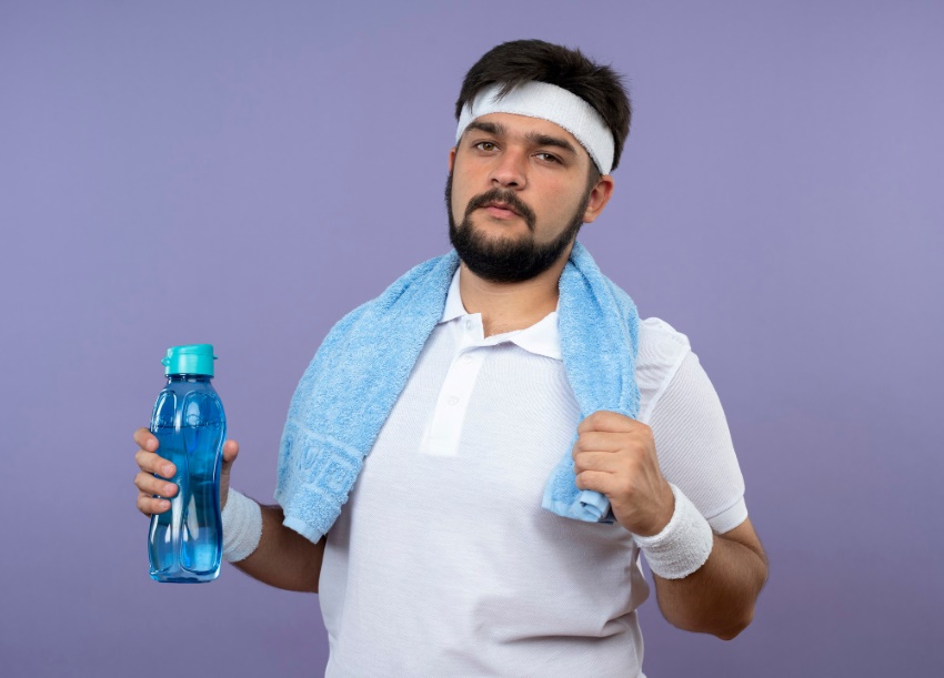 confident-young-sporty-man-wearing-headband-wristband-with-towel-shoulder-holding-water-bottle