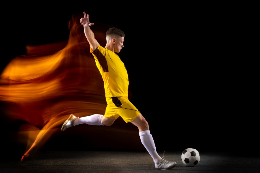 young-caucasian-male-football-soccer-player-kicking-ball-goal-mixed-light-dark-wall-concept-healthy-lifestyle-professional-sport-hobby